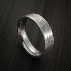 May include: A silver wedding band with a unique, patterned design. The band is made of metal and has a smooth, polished finish.
