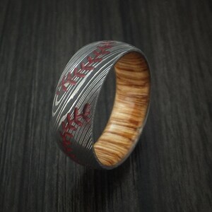 Puede incluir: Un anillo de madera con un patr&oacute;n negro y plateado, que se asemeja a una pelota de b&eacute;isbol, con costuras rojas.