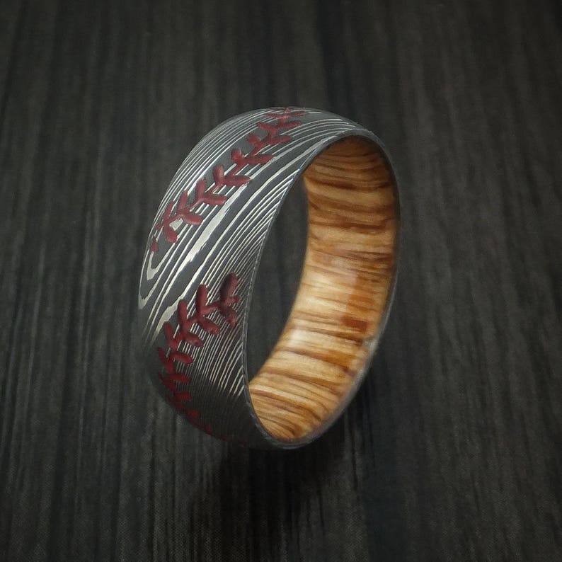 Puede incluir: Un anillo de madera con un patr&oacute;n negro y plateado, que se asemeja a una pelota de b&eacute;isbol, con costuras rojas.