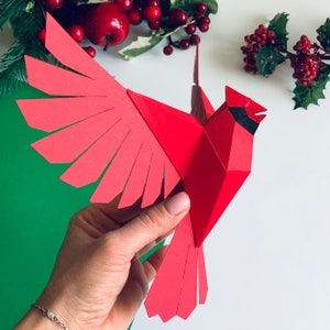 Pu&ograve; includere: Un cardinale di carta rosso con occhi neri e becco nero. Il cardinale &egrave; in volo con le ali spiegate. Il cardinale &egrave; fatto di carta ed &egrave; un modello di origami 3D.