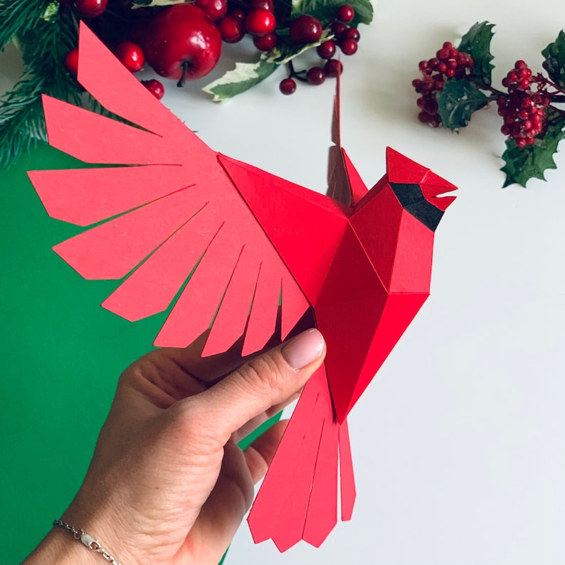 Pu&ograve; includere: Un cardinale di carta rosso con occhi neri e becco nero. Il cardinale &egrave; in volo con le ali spiegate. Il cardinale &egrave; fatto di carta ed &egrave; un modello di origami 3D.