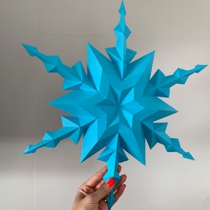May include: A large, blue, paper snowflake with a 3D design. The snowflake is made of many small triangles and has a pointed star shape in the center.