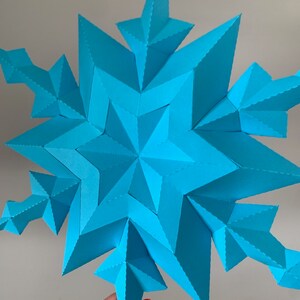 May include: A large, blue paper snowflake with a 3D design. The snowflake is made of many folded pieces of paper, creating a complex and intricate pattern.