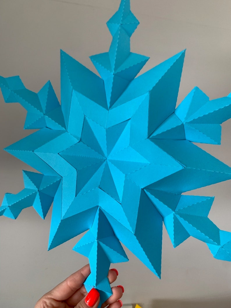 May include: A large, blue paper snowflake with a 3D design. The snowflake is made of many folded pieces of paper, creating a complex and intricate pattern.