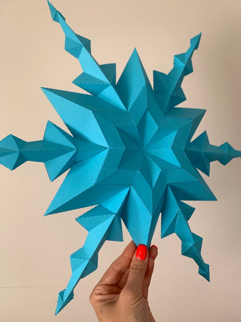 May include: A large, blue, paper snowflake with a 3D design. The snowflake is made of many small triangles and has a starburst shape.