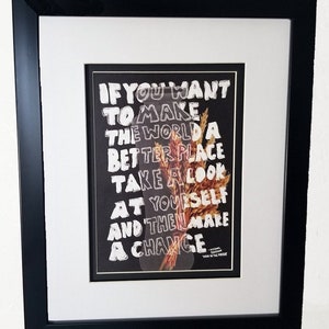 Könnte beinhalten: Gerahmter Druck mit schwarzem Hintergrund und weißem Text, der lautet: "Wenn du die Welt zu einem besseren Ort machen willst, schau dich selbst an und dann mach eine Veränderung." Der Text ist mit einem Trockenblumenarrangement überlagert.
