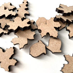 May include: A collection of wooden craft shapes in the form of leaves and acorns. The shapes are light brown and have a dark brown outline.