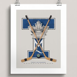 May include: A vintage-style poster featuring a blue and white "T" with a maple leaf and a hockey stick design. The text "STANLEY CUP CHAMPIONS" is at the bottom of the poster, with a list of years from 1918 to 1967.