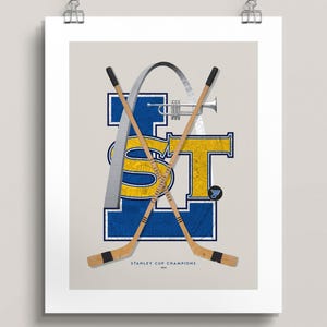 May include: A blue and yellow graphic with the letters "STL" and a silver archway. Two hockey sticks are crossed behind the letters. The text "STANLEY CUP CHAMPIONS 2019" is below the graphic.