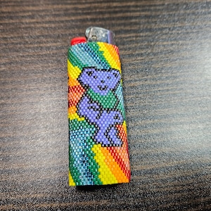 May include: A rainbow-colored beaded lighter case with a purple bear graphic.