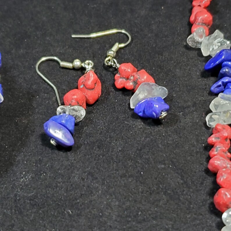 May include: A pair of earrings and a necklace made with red, white, and blue gemstone beads. The earrings have silver hooks and the necklace has a silver clasp.