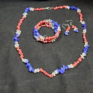 May include: A red, white, and blue gemstone necklace, bracelet, and earrings set. The jewelry is made of small, irregular shaped stones.