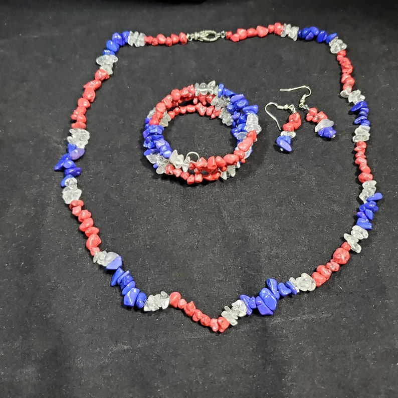May include: A red, white, and blue gemstone necklace, bracelet, and earrings set. The jewelry is made of small, irregular shaped stones.