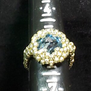 May include: A gold ring with a blue gemstone surrounded by gold beads.