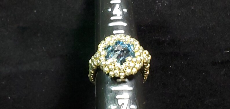 May include: A gold ring with a blue gemstone surrounded by gold beads.