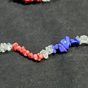 May include: A close-up of a red, white, and blue beaded necklace. The beads are irregular in shape and size, and they are strung together on a clear thread.