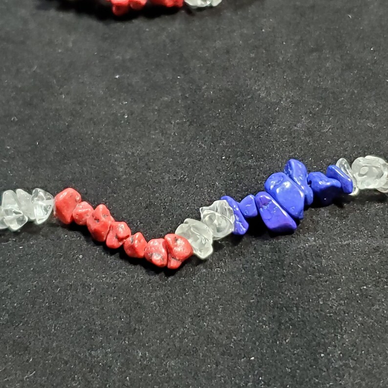 May include: A close-up of a red, white, and blue beaded necklace. The beads are irregular in shape and size, and they are strung together on a clear thread.
