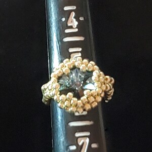 May include: A gold ring with a large, clear, faceted gemstone set in the centre. The ring is on a ruler, showing the size of the ring.