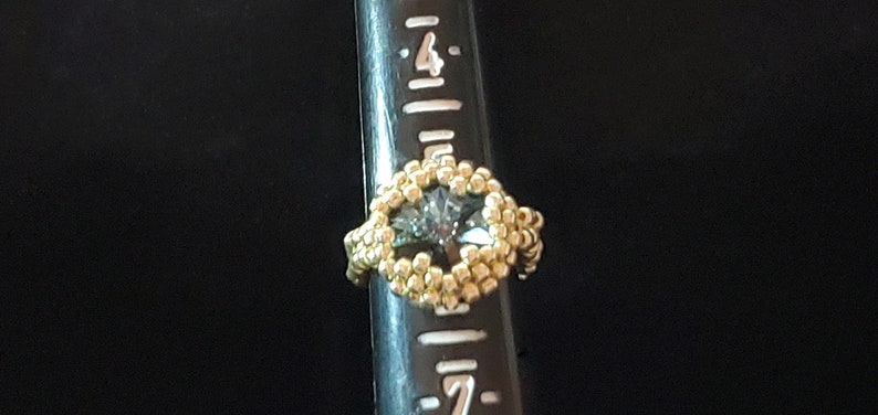 May include: A gold ring with a large, clear, faceted gemstone set in the centre. The ring is on a ruler, showing the size of the ring.