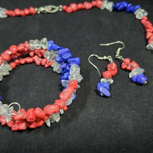 May include: A red, white, and blue gemstone necklace, bracelet, and earrings set. The jewelry is made of small, irregular shaped stones.