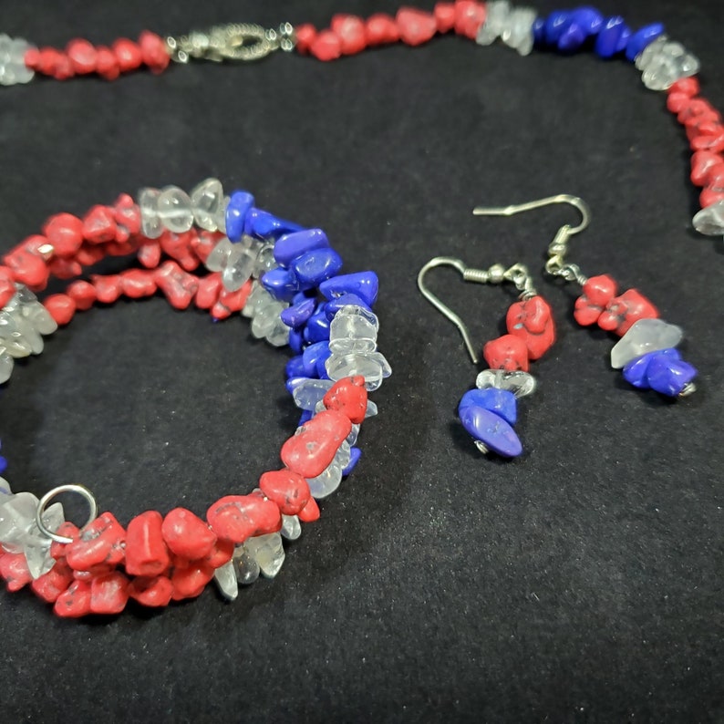 May include: A red, white, and blue gemstone necklace, bracelet, and earrings set. The jewelry is made of small, irregular shaped stones.