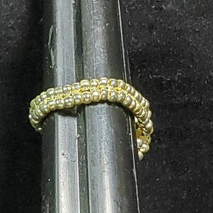May include: A gold beaded ring with a simple design, shown against a black background.