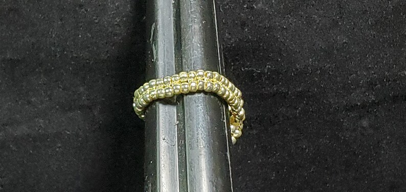 May include: A gold beaded ring with a simple design, shown against a black background.
