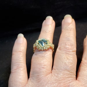 May include: A gold ring featuring a large, faceted, blue gemstone surrounded by smaller gold beads.