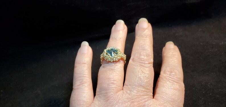 May include: A gold ring featuring a large, faceted, blue gemstone surrounded by smaller gold beads.