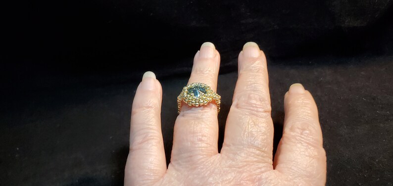 May include: A gold ring with a dark blue gemstone set in a beaded design.