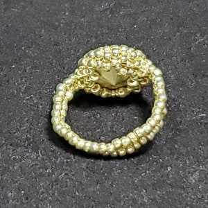 May include: A gold beaded ring with a round, beaded centre piece.