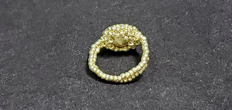 May include: A gold beaded ring with a round, beaded centre piece.