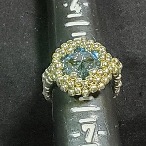 May include: A gold beaded ring with a large blue gemstone in the centre.