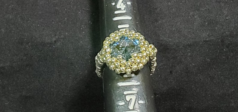 May include: A gold beaded ring with a large blue gemstone in the centre.