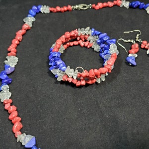 May include: A set of red, white, and blue gemstone jewelry, including a necklace, bracelet, and earrings. The jewelry is made of small, irregular shaped stones.