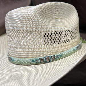 May include: A light beige straw cowboy hat with a beaded band in shades of green and brown.