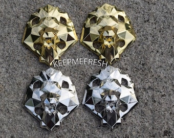 May include: Four decorative lion head ornaments, two gold and two silver, with a geometric design. The ornaments have a 3D effect and are made of a shiny material.