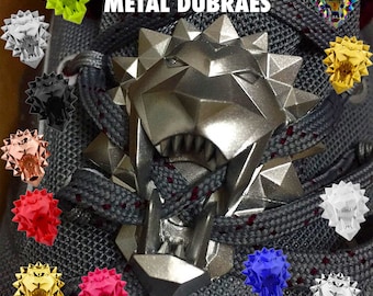 May include: A close-up of a pair of trainers with a silver metal lion head shoelace charm. The charm has a spiky design and is attached to the laces. The trainers are grey and have red laces. The image also shows a variety of other lion head charms in different colours, including gold, red, blue, black, white, and green.