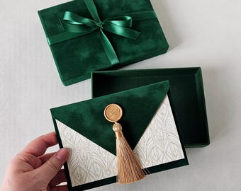 May include: A dark green velvet box with a matching satin ribbon bow, paired with a matching dark green velvet envelope featuring a gold wax seal, a gold tassel, and a white card insert with a gold geometric line pattern printed on the surface.