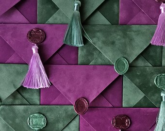 May include: A collection of overlapping envelopes in deep purple and forest green suede-like material. Each envelope is secured with a decorative wax seal in a matching color, featuring an attached silk tassel that hangs from the center point.