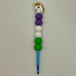 May include: A blue crochet hook with a unicorn head topper. The hook has purple, white, and green beads.
