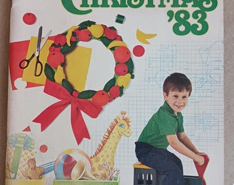 May include: A vintage magazine cover with the text "Have a Natural Christmas '83". The cover features a Christmas wreath, a toy train, and a young boy. The train has a giraffe and other toys. The boy is sitting on a toy train.