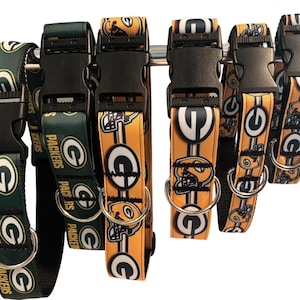 May include: A collection of six dog collars featuring the Green Bay Packers logo and team colors of green, gold, and white. Each collar is equipped with a black plastic side-release buckle and a silver metal D-ring for leash attachment.