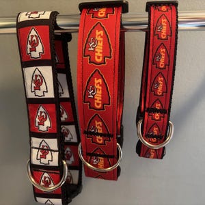 Puede incluir: Tres collares de perro rojos, blancos y negros con las palabras "KC Chiefs" impresas en ellos. Los collares est&aacute;n colgados de una barra de metal.