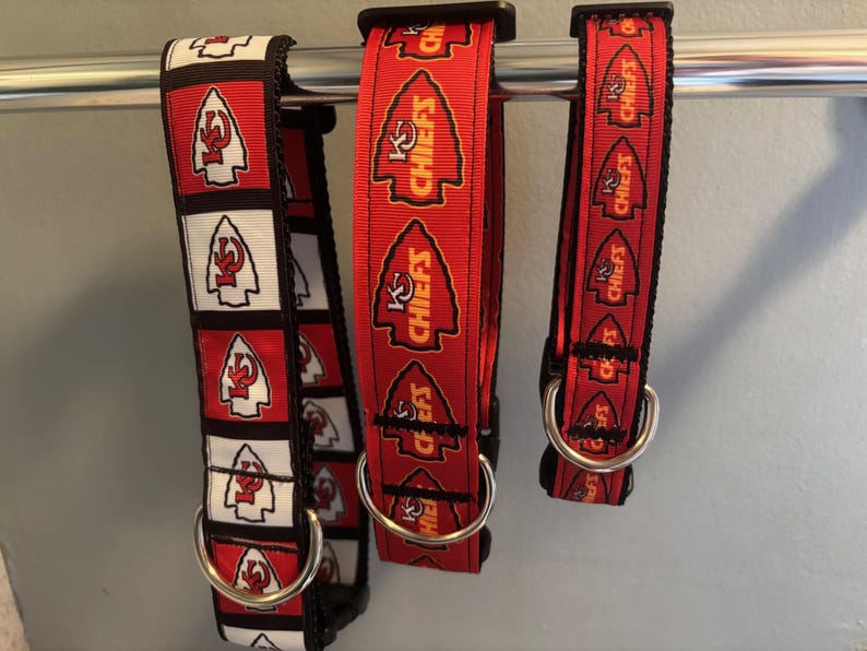Puede incluir: Tres collares de perro rojos, blancos y negros con las palabras "KC Chiefs" impresas en ellos. Los collares est&aacute;n colgados de una barra de metal.