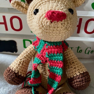 May include: A crocheted reindeer toy with brown antlers, a red nose, and a green and red striped scarf.