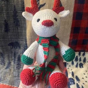 May include: White crocheted reindeer with red antlers, green and red striped scarf, and red crocheted feet.