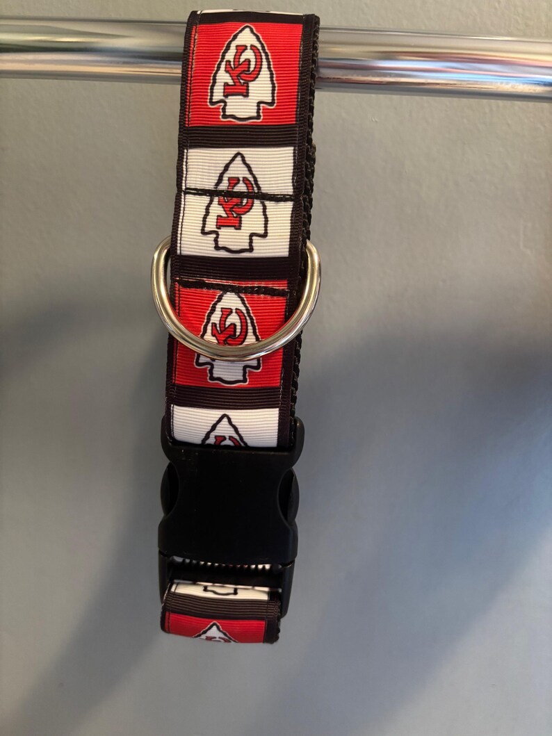 Puede incluir: Un collar de perro rojo, blanco y negro con un patr&oacute;n repetido del logotipo de los Kansas City Chiefs. El collar tiene un anillo en D plateado y una hebilla de pl&aacute;stico negra.