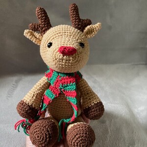 May include: A crocheted reindeer toy with brown antlers, a red and green striped scarf, and brown hooves.