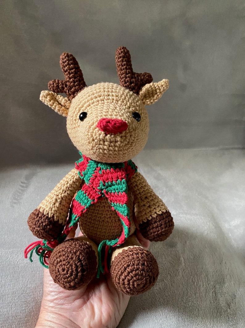 May include: A crocheted reindeer toy with brown antlers, a red and green striped scarf, and brown hooves.